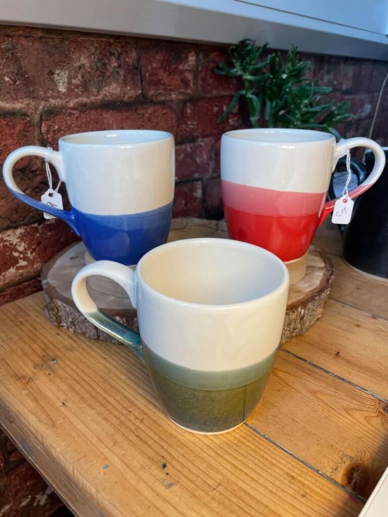 a blue and white, red and white, and green and white mug made by Ciaran Headley of CH Pottery