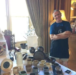 A picture of Ciaran Headley, owner of CH Pottery, standing beside a table of his ceramics.