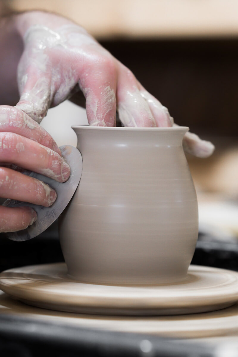 a person working clay into a pot using a potter's wheel